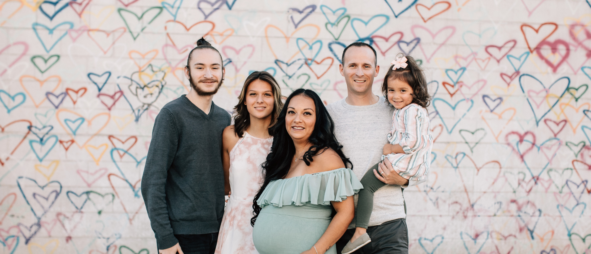 Multi-Generational Family in front of a wall with multi-colored hearts painted on it.